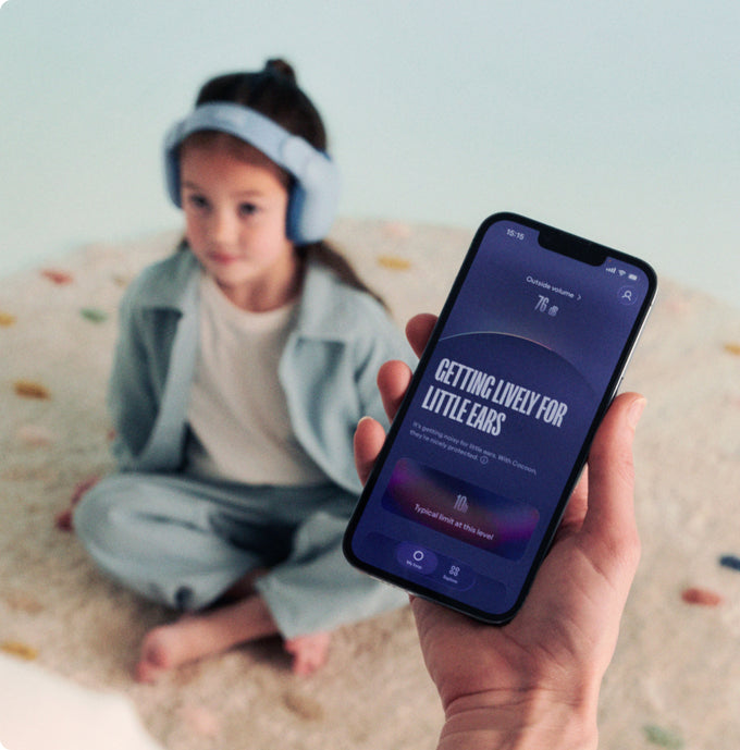 Child wearing Loop earmuffs with a phone displaying an app interface on a light background