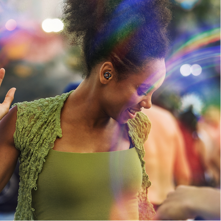 Woman wearing a green top and green cardigan with a blurred colorful festival background