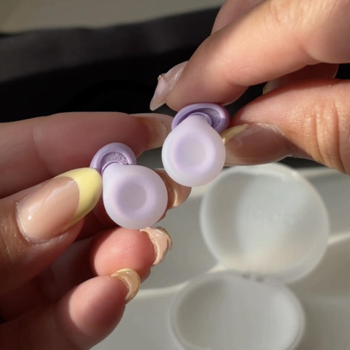 A close-up of hands holding a pair of Loop Dream earplugs.
