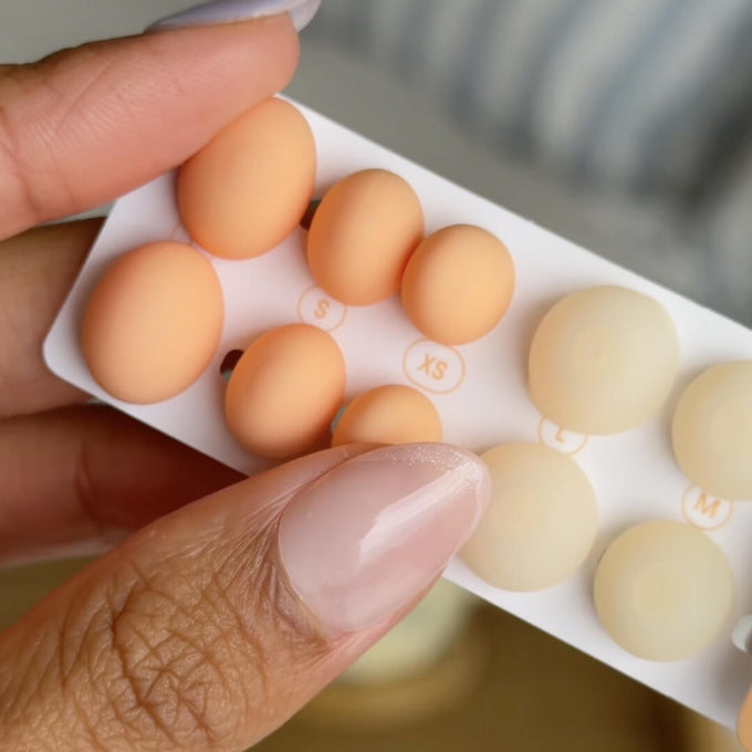 A close-up of a hand holding a white card displaying Loop Dream ear tips in different sizes for XS to L